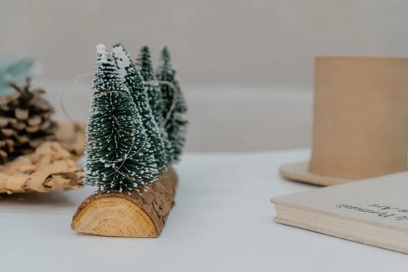 A charming still life featuring miniature Christmas trees on a wooden base amidst warm, earthy tones, creating a festive ambiance