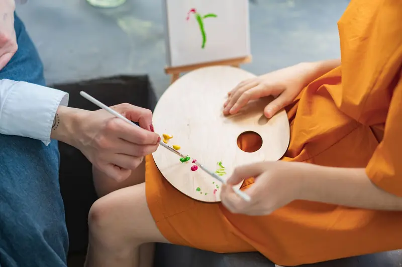 Creative close-up of hands painting using a palette and brush. Art creation at an indoor setting