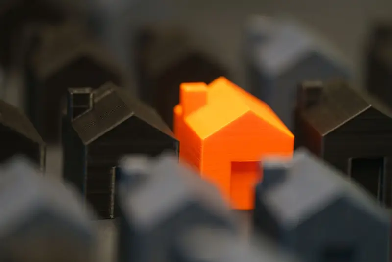 A vibrant orange model house stands out among black miniature houses, symbolizing real estate concepts