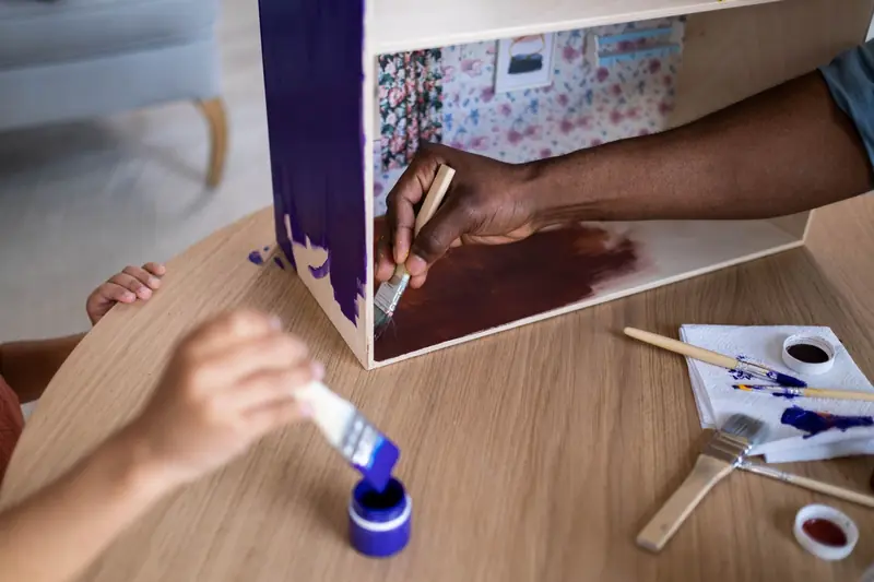 Adults and child creatively painting a wooden dollhouse using vibrant colors and brushes