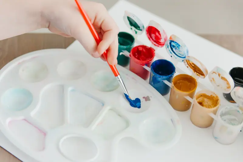 Close-up of a hand painting with vibrant acrylic colors on a palette, showcasing artistic creativity