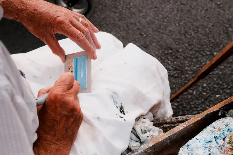 Close-up of an elderly man painting a miniature seascape in Normandie, France outdoors
