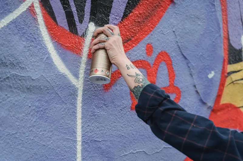 Close-up of a tattooed hand creating colorful street art with spray paint on a wall