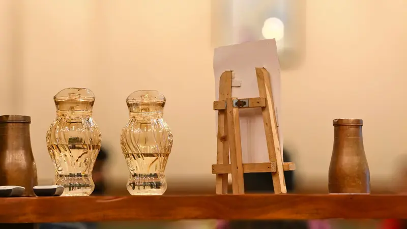 A warm and rustic still life featuring a miniature easel alongside decorative glass jars on a wooden shelf