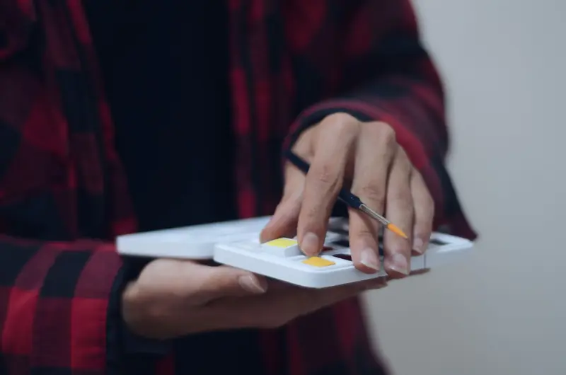 Close-up of person holding a paint palette and brush indoors, creating art
