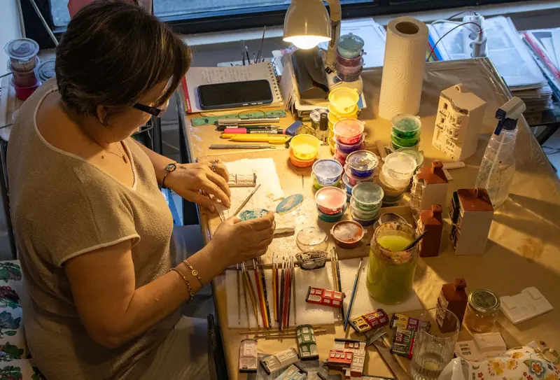 Woman sculpting and painting miniature houses in a cozy indoor studio