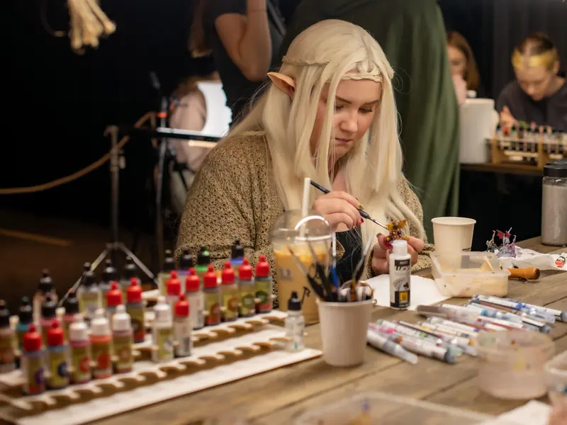 A woman cosplays as an elf while painting miniatures at an indoor convention