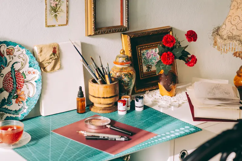 A cozy artist's workspace featuring painting supplies, decor, and floral accents on a desk