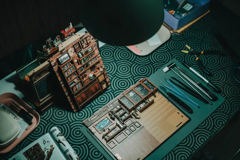 A detailed miniature bookshelf crafting setup with tools on a patterned table