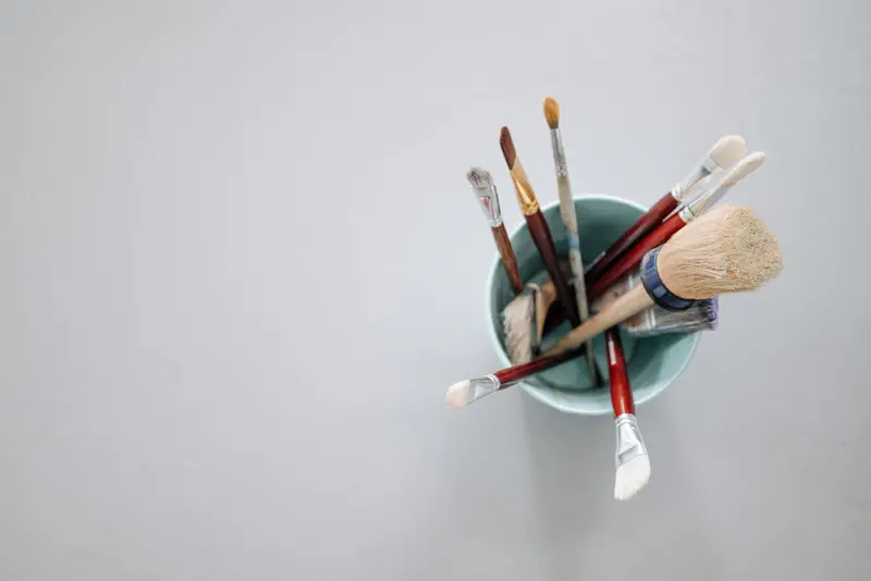 Assorted paint brushes in a blue cup against a light background, top view