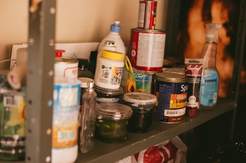 A cluttered shelf in a workshop stocked with various paint containers and supplies
